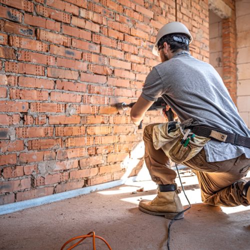 handyman-at-construction-site-in-the-process-of-drilling-wall-with-perforator